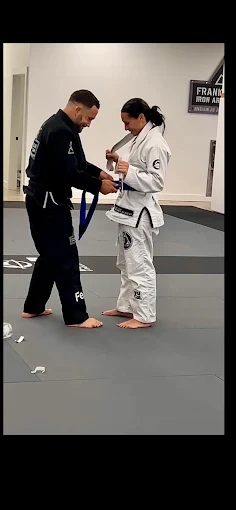 A coach tying a new belt on a student at the academy